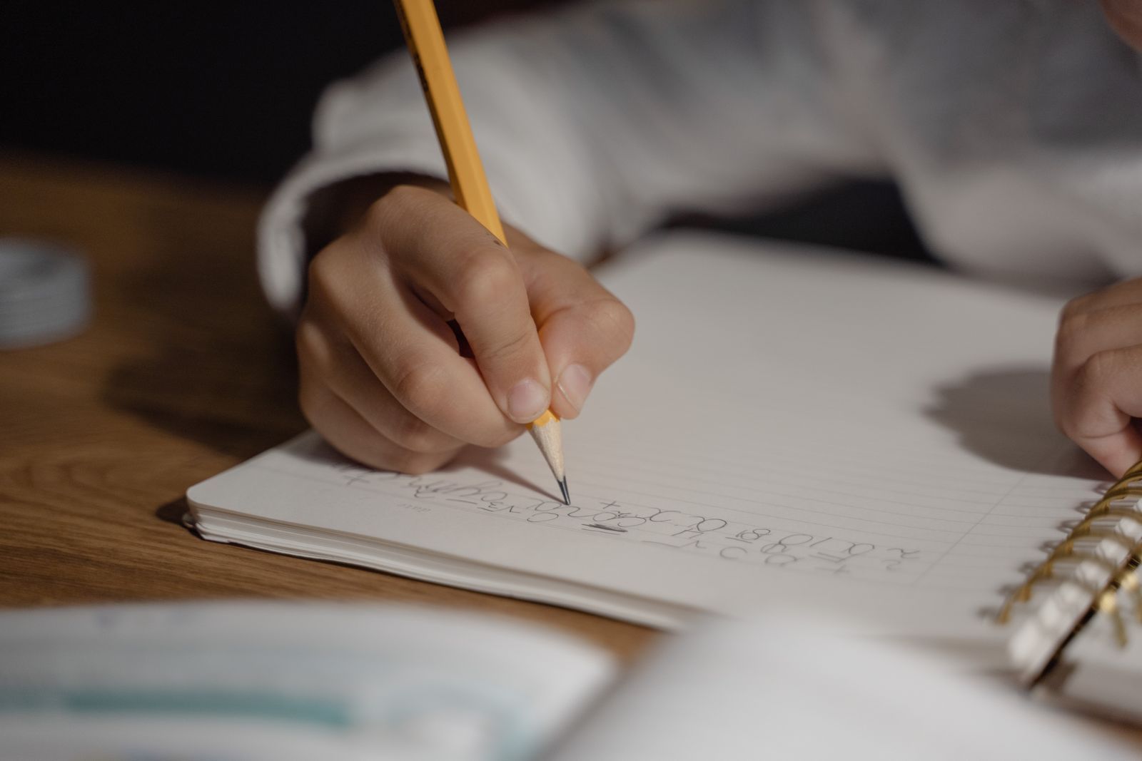 Mão de criança escrevendo no caderno com lápis